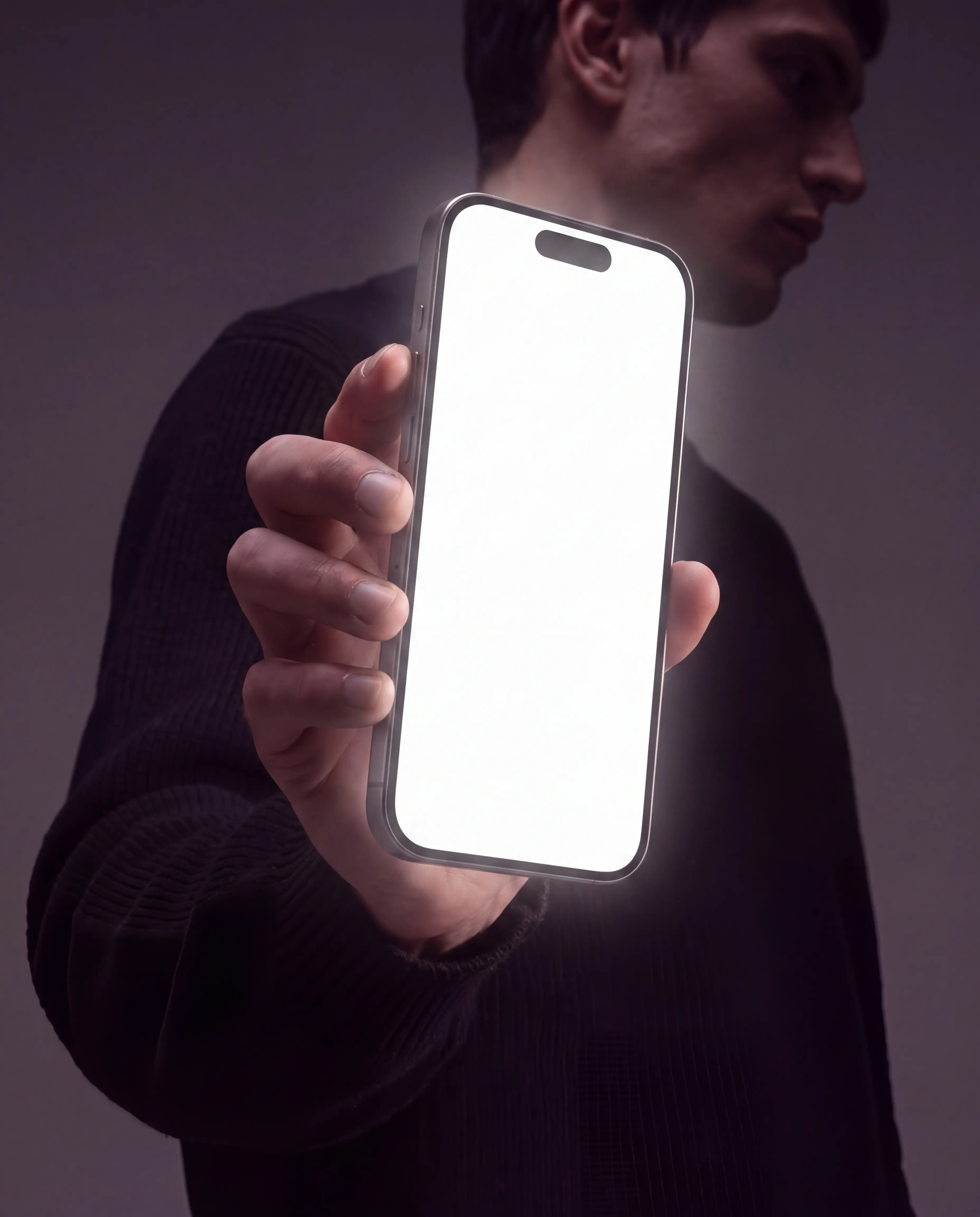 Silver iPhone held upright close to the camera by a man wearing a black sweater in a moody violet-grey studio portrait, with an editable white vertical display and visible Dynamic Island
