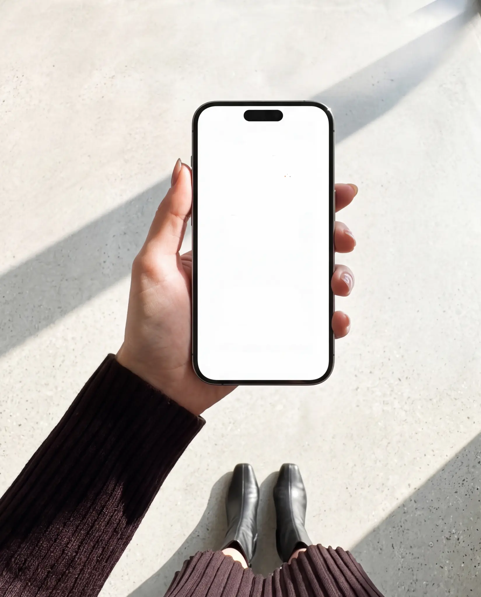 Realistic iPhone screen mockup held in hand with natural sunlight Modern black iPhone held upright in one hand against a bright concrete floor with strong diagonal sunlight and an editable white screen with Dynamic Island